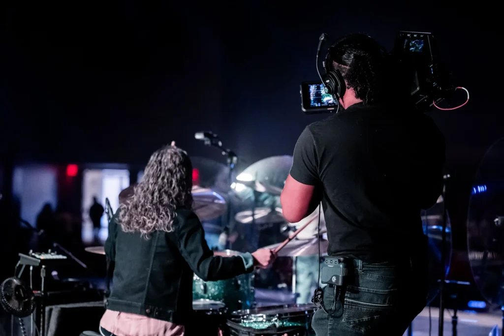 Behind the scenes of a music video production process, a camera operator is filming a performer.